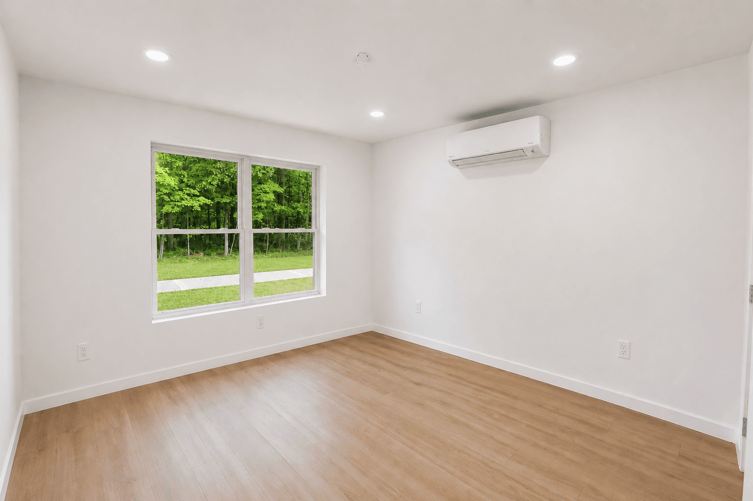 Tillson Woods bedroom with light wood-tone flooring, windows, and a wall-mounted mini-split system.